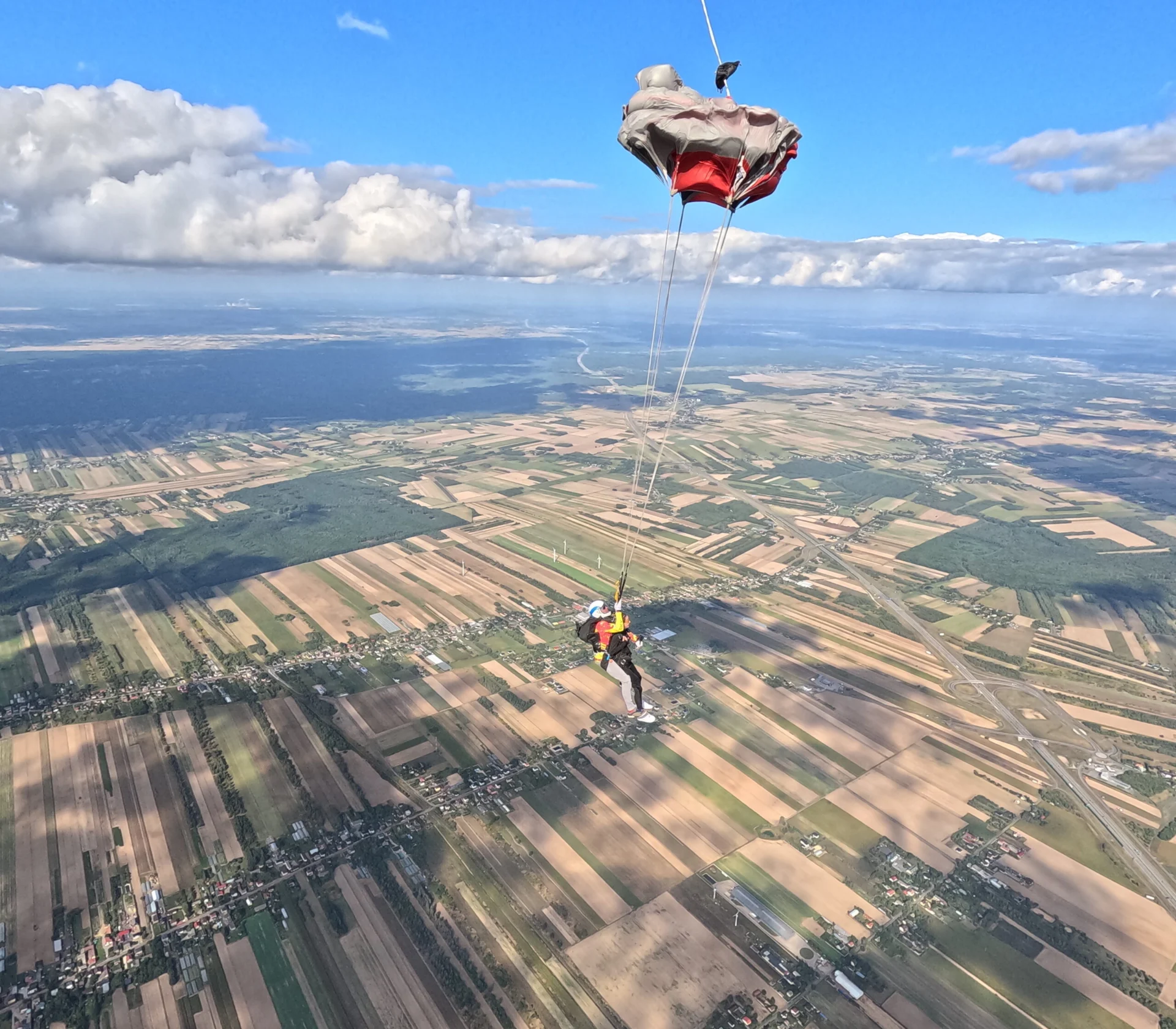 Otwarcie czerwono-białego spadochronu tandemowego nad polami.