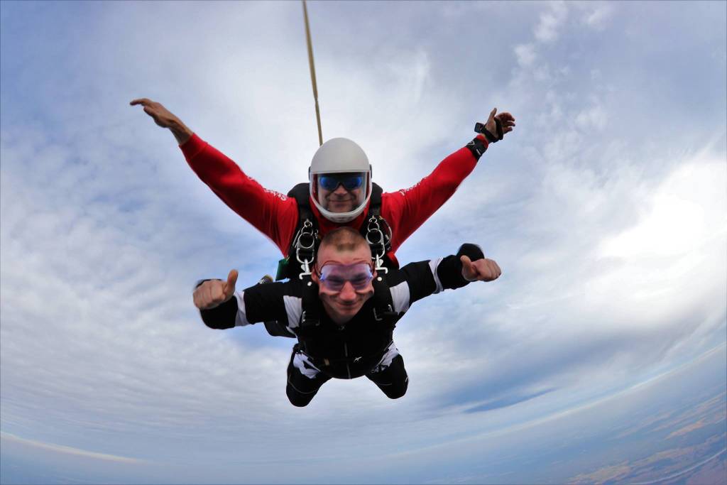 Dwóch mężczyzn leci w powietrzu i są przypięci do spadochronu.
